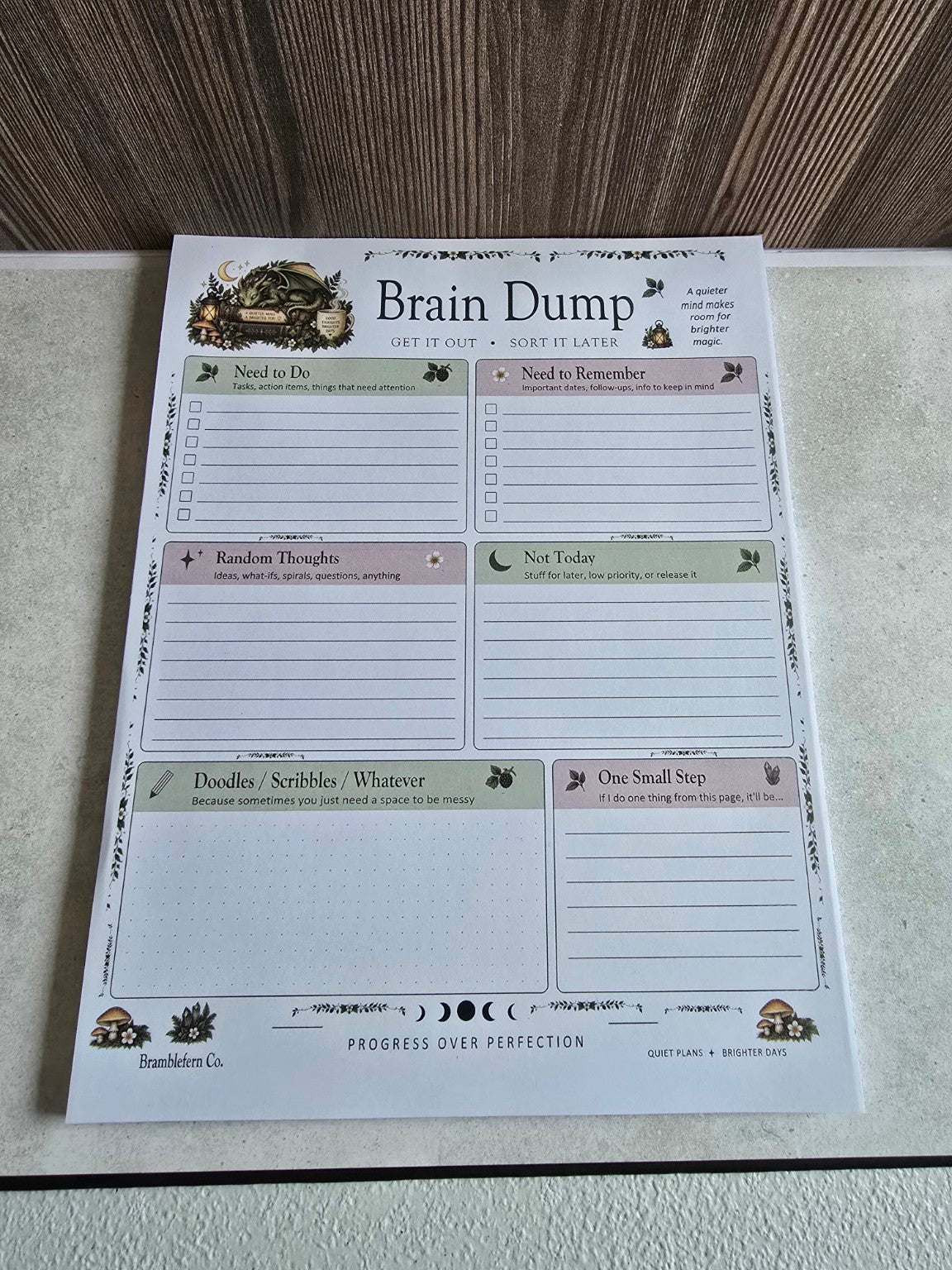 Angled view of the Brain Dump notepad showing woodland dragon and six-section planner layout