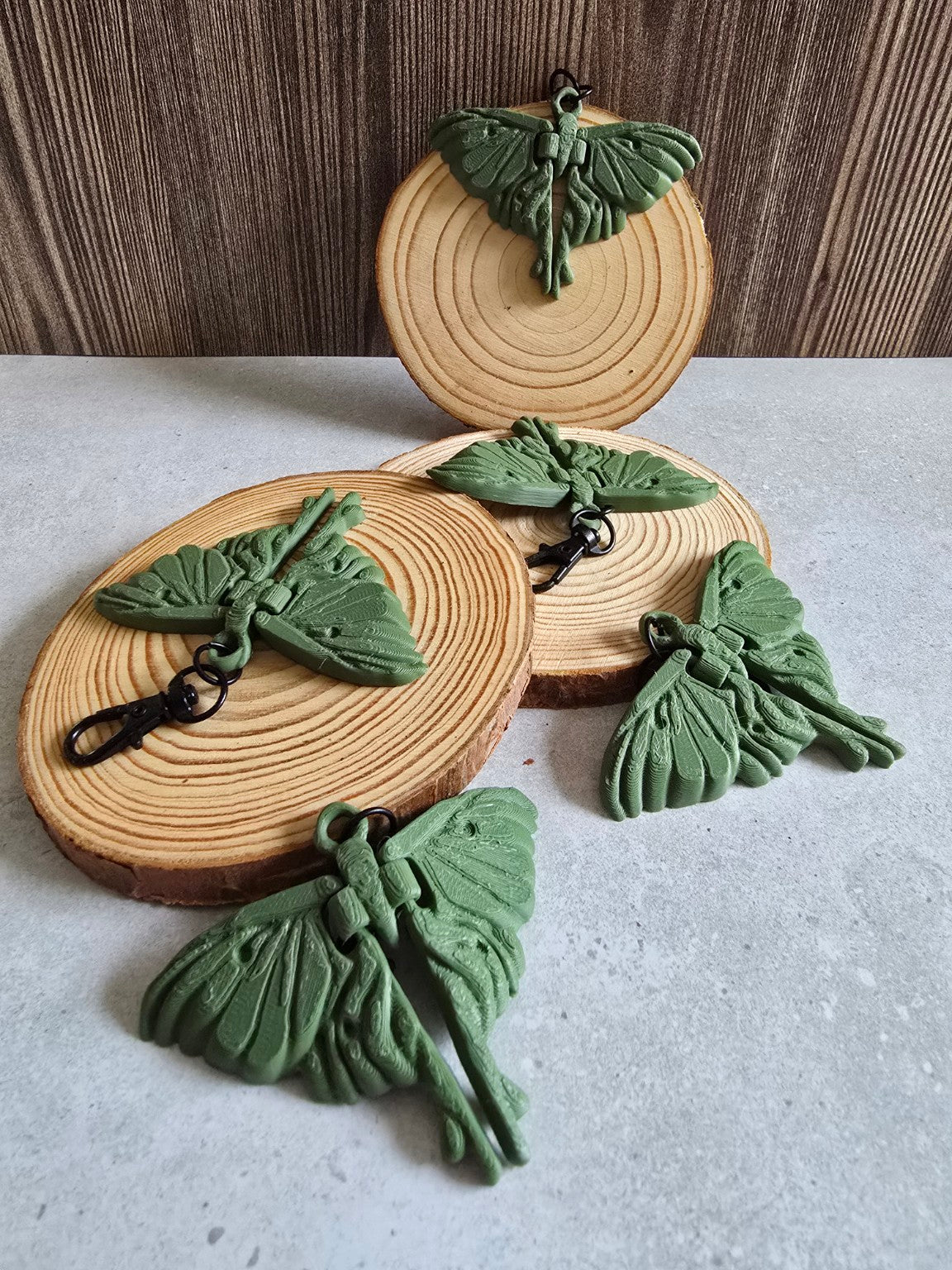 Four olive green moth keychains displayed on wooden slices