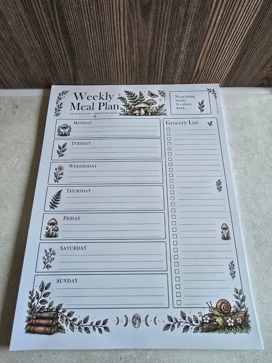 Angled view of the woodland Weekly Meal Planner notepad with botanical details, moon phases and snail