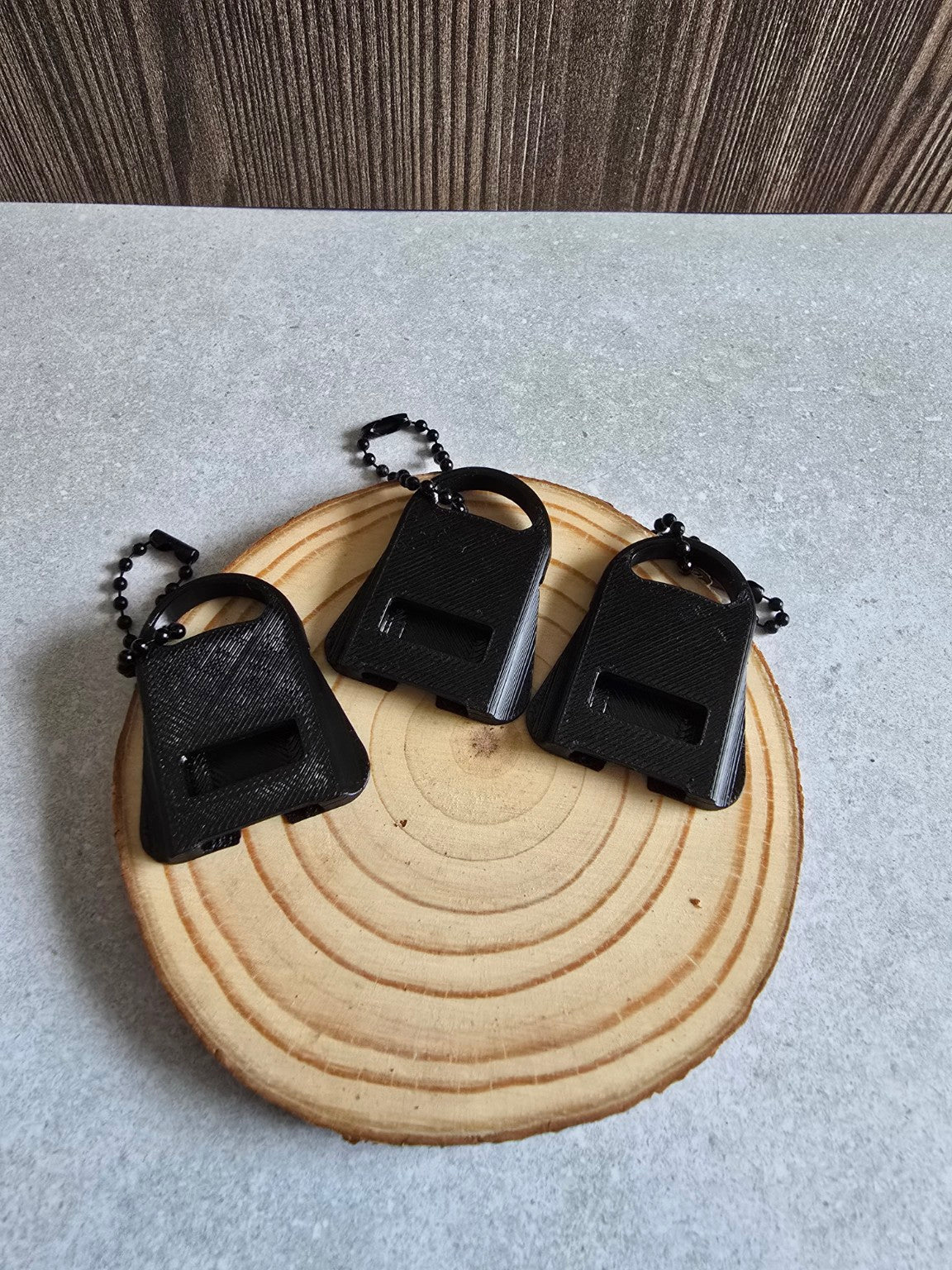 Three black PETG can tab opener keychains displayed on a wood slice