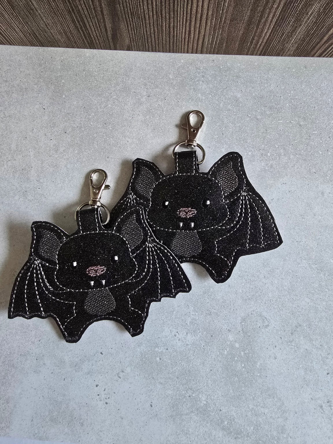 Two matching black embroidered bat sanitizer holders with metal swivel clips, showing the two remaining pieces.