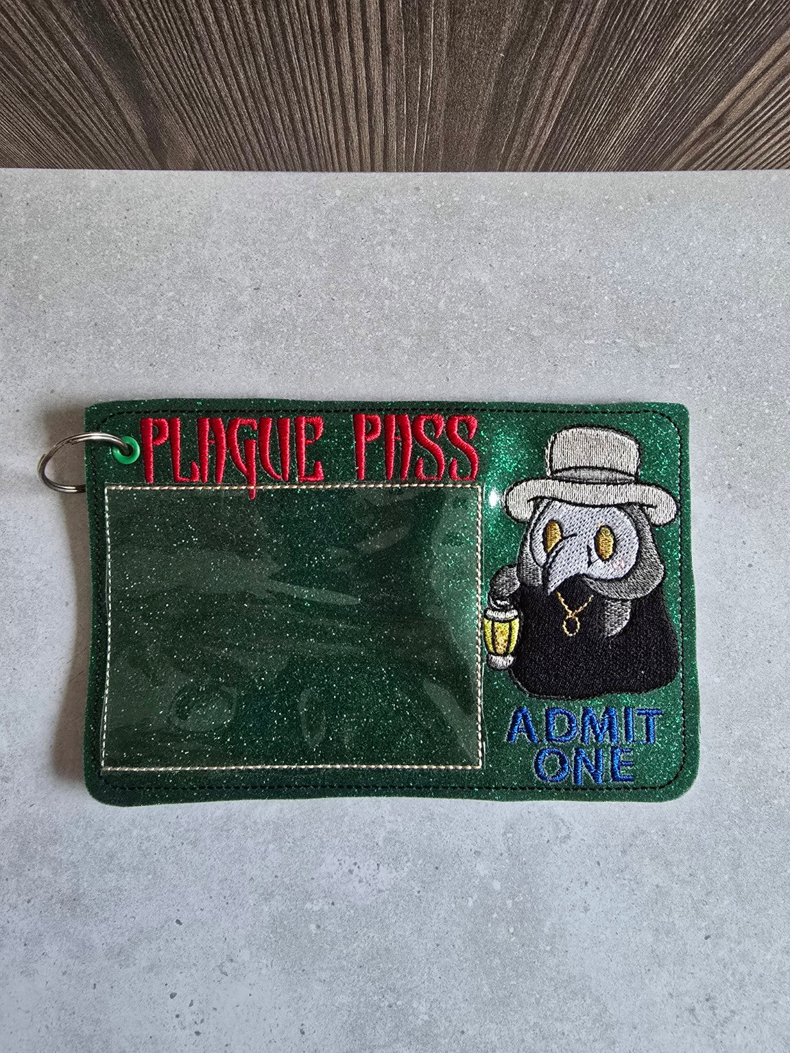 Copper-orange glitter plague doctor pass holder standing upright, showing red Plague Pass lettering and stitched clear pocket.
