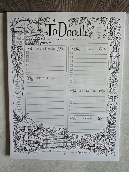 ToDoodle woodland daily planner and coloring notepad, front view with sleeping cat on books, moth, lantern, mushrooms and planning boxes