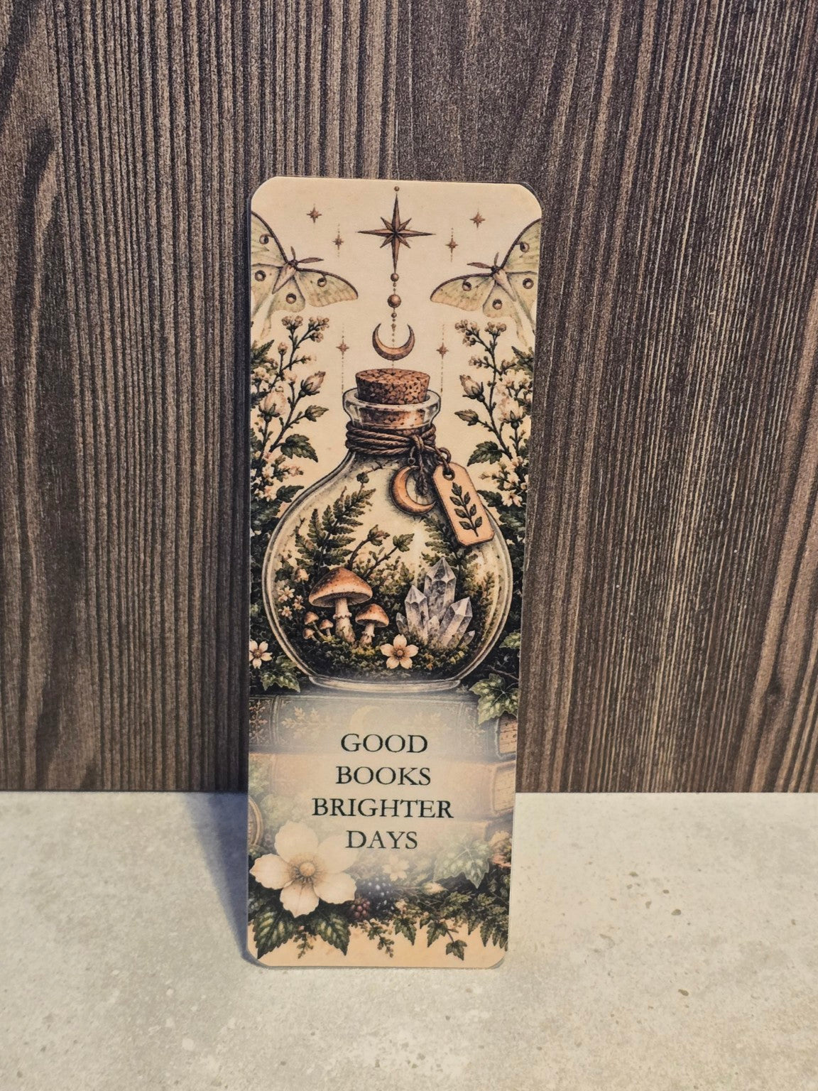Good Books Brighter Days laminated bookmark featuring a woodland terrarium bottle, mushrooms, crystals, moths, and celestial details.