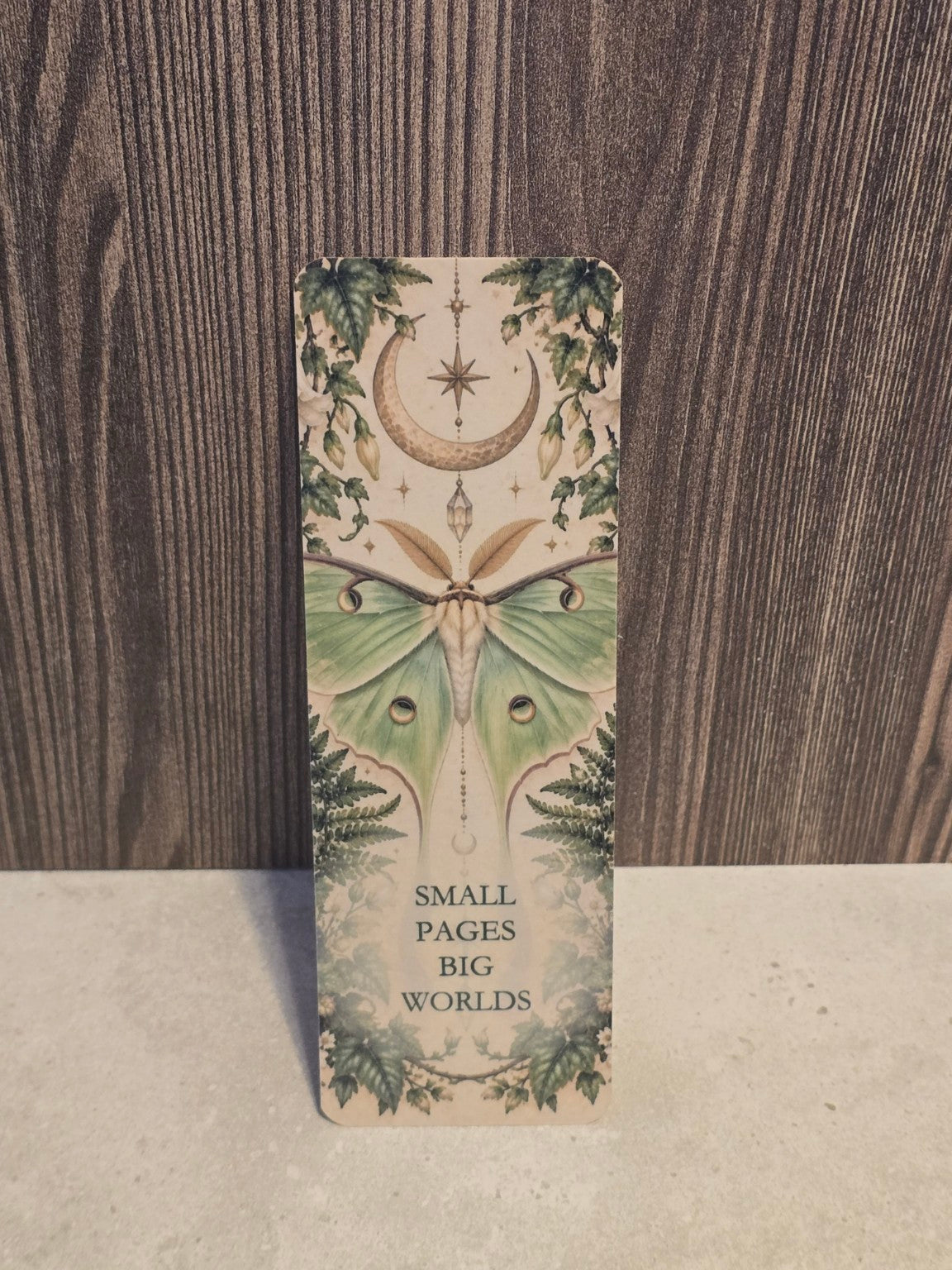 Small Pages Big Worlds laminated bookmark with a pale green luna moth, crescent moon and leafy botanical artwork.