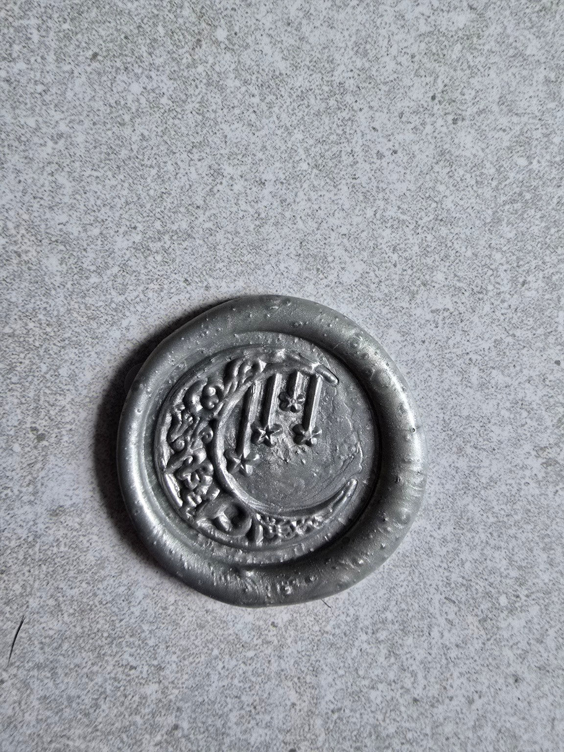 Close-up of a handmade wax seal with moon and stars design.