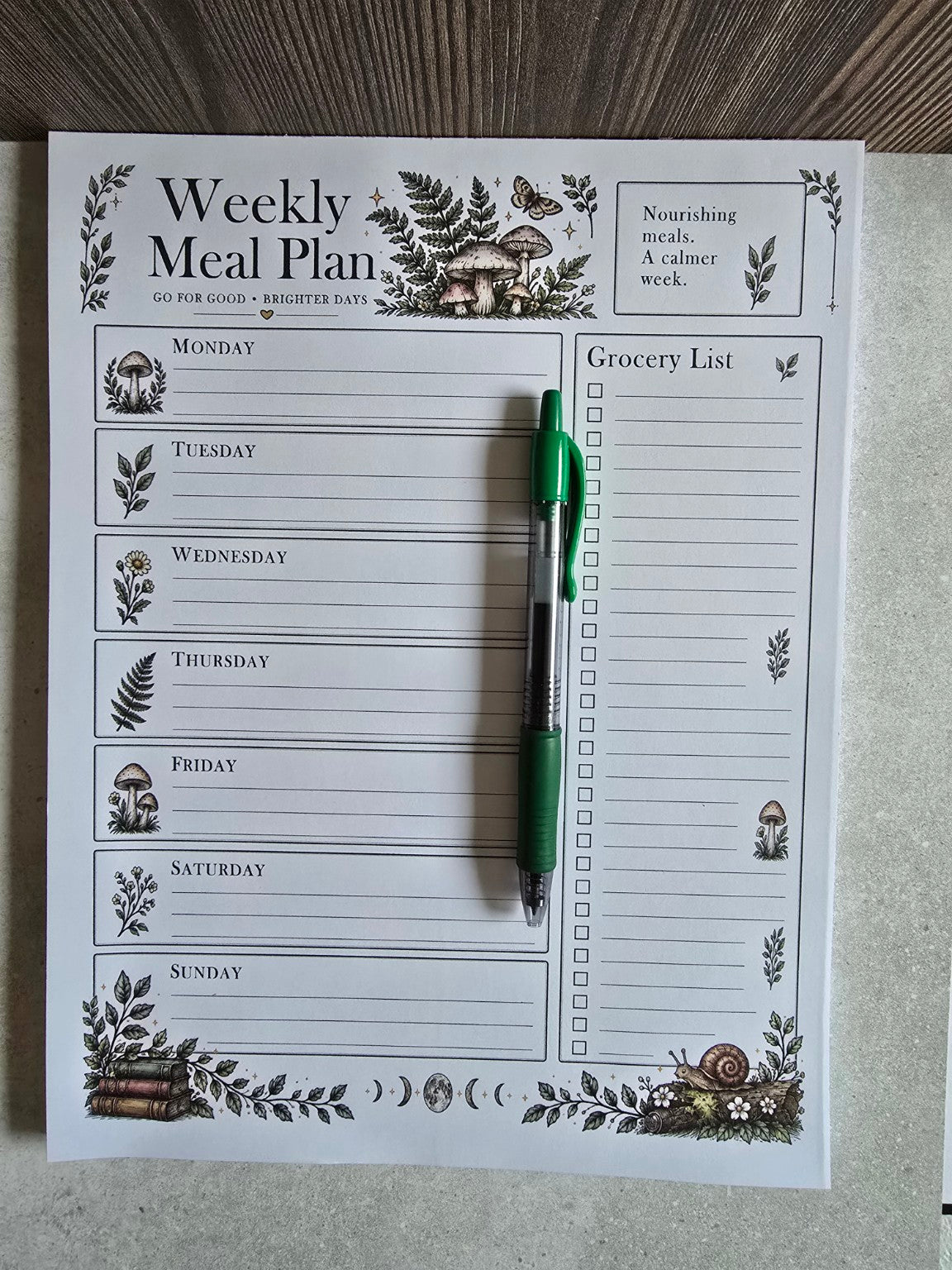 Weekly Meal Planner notepad shown with green pen for scale, grocery checklist and seven-day meal planning